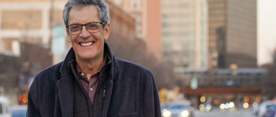 Jeff Boarini smiling on a downtown street at dusk, with tall buildings and traffic lights behind him